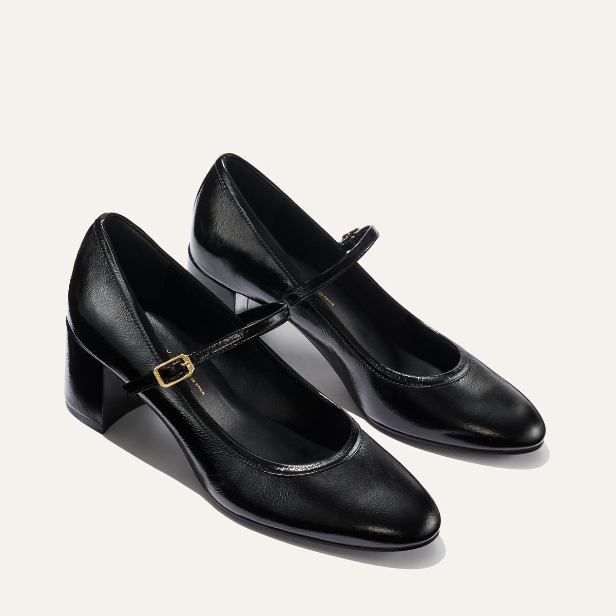 The Mira Jane - Black Crinkle Patent by margaux-development features classic Mary Jane style with black leather, rounded toes, mid-height block heels, and gold buckles on slim straps, shown against a neutral background.