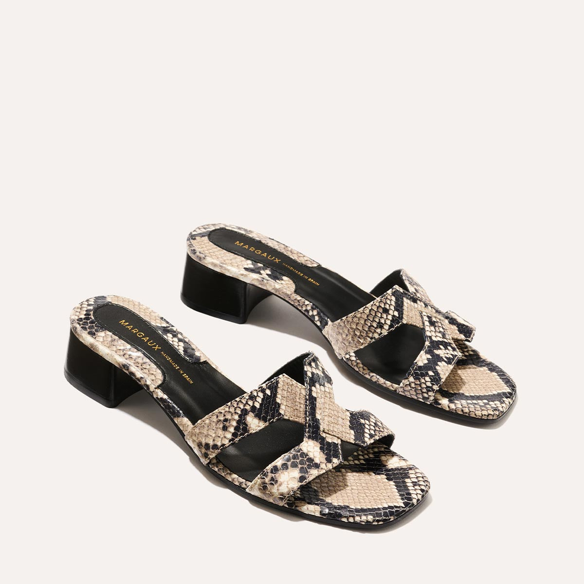 The MX 35 - Natural Python Embossed by margaux-development elevates the classic MX Sandal with open-toe block heels, crisscross straps, a beige and black snakeskin pattern, and a black insole with gold branding.