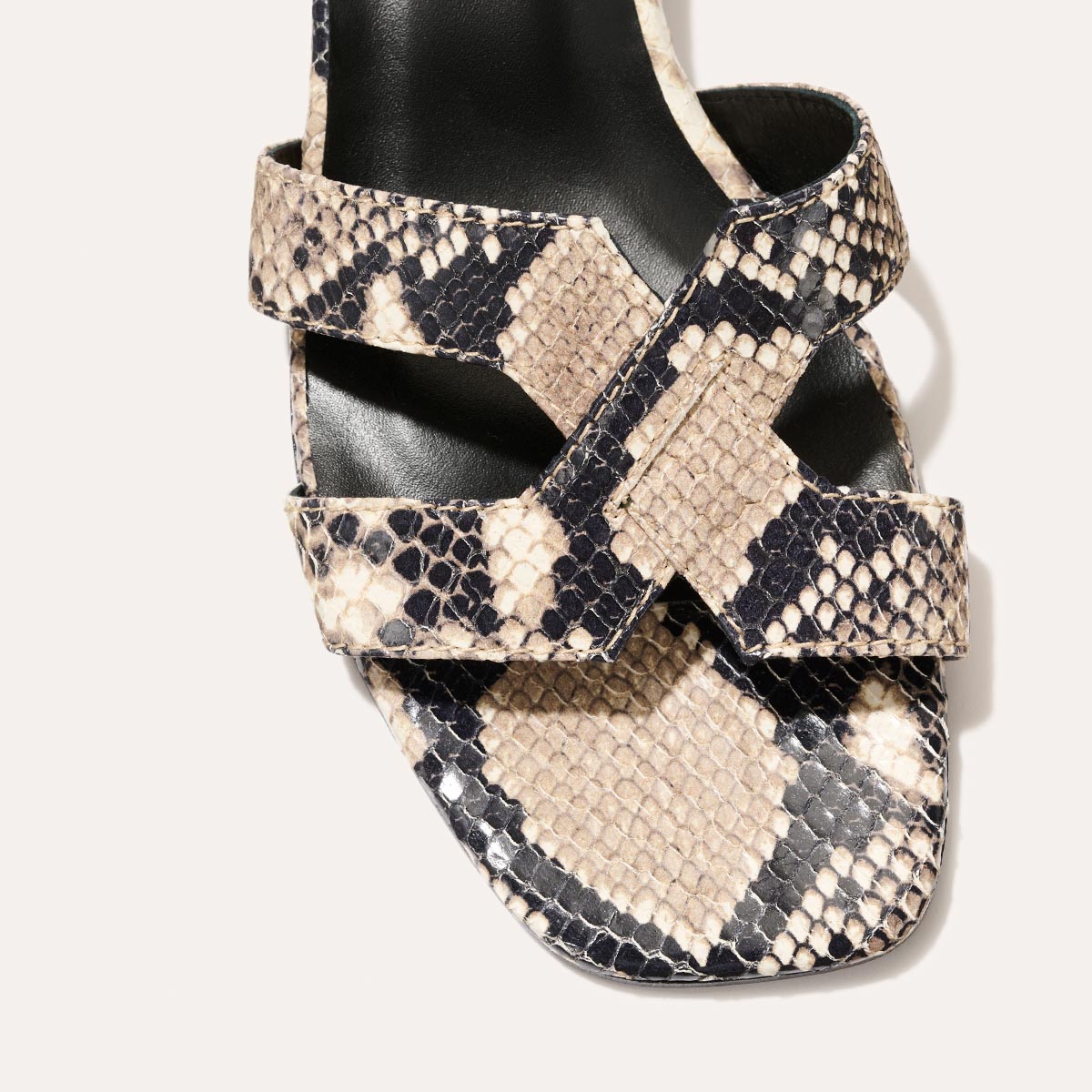 A close-up of The MX 35 - Natural Python Embossed by margaux-development, featuring black, beige, and cream snake-print crisscross straps over a square open toe and an elevated block heel for added style.
