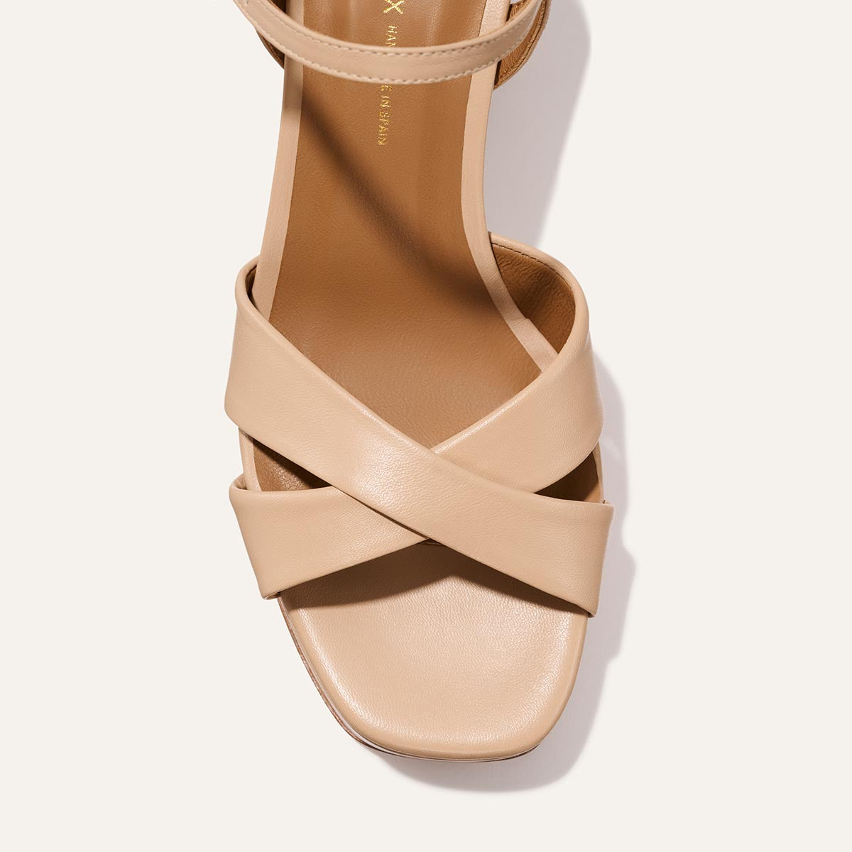 A top-down view of Margaux’s The Paloma Platform in Dune Nappa: a beige padded sandal with wide crisscross leather straps and a square open toe, designed for all-night comfort, set against an off-white background.
