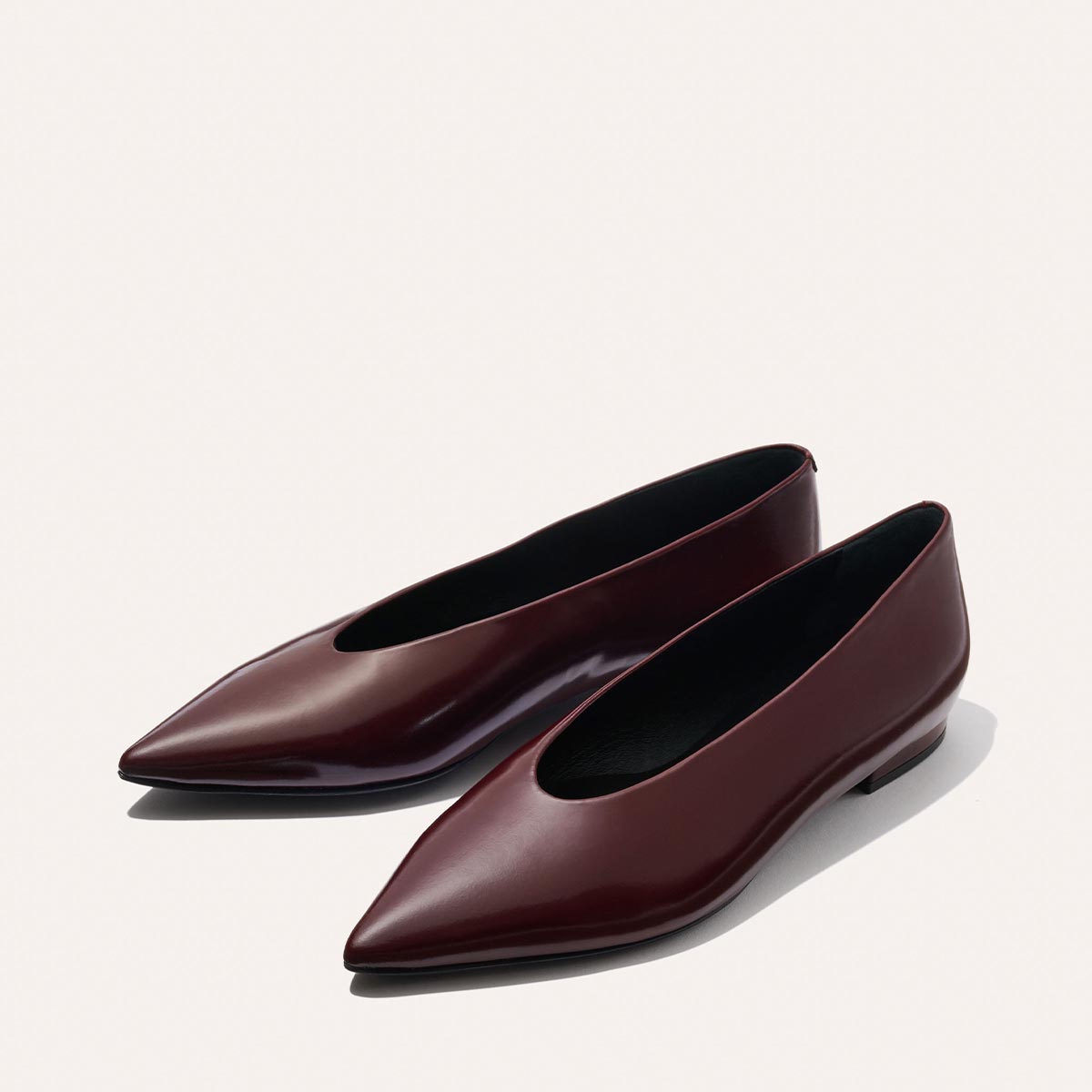 The Parra - Burgundy Calf by margaux-development: sleek, pointed-toe burgundy leather flats with a structured silhouette, low heel, and glossy finish, shown side by side on a light neutral background.