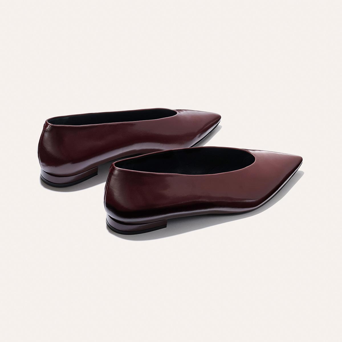 The Parra - Burgundy Calf by margaux-development: sleek, minimalist pointed-toe flats in shiny burgundy leather with low heels and a structured silhouette, shown against a plain light background.
