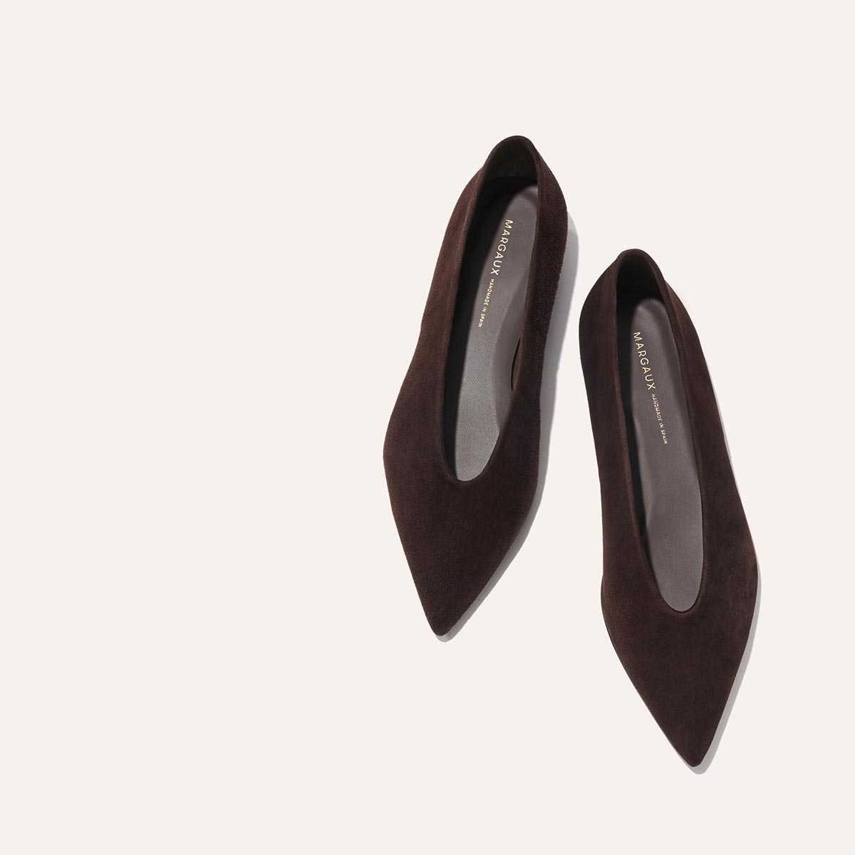The Parra - Espresso Suede flats by margaux-development are displayed on a light beige background, one shoe slightly angled toward the other, highlighting their dark brown pointed-toe suede design.