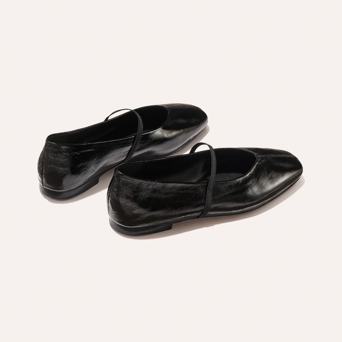 The Phoebe - Black Crinkle-Gloss Nappa by margaux-development: shiny black ballet flats with thin top straps, crafted with sacchetto construction for flexibility, shown on a plain light background.