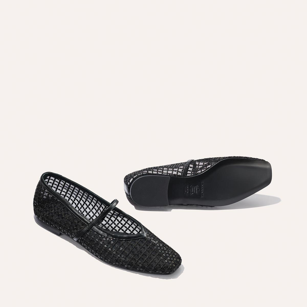 The Phoebe - Black Sequin Mesh by margaux-development: a pair of black mesh Mary Jane flats with a sparkling textured finish, shown with one shoe upright and the other overturned to display the sole on a plain light background.