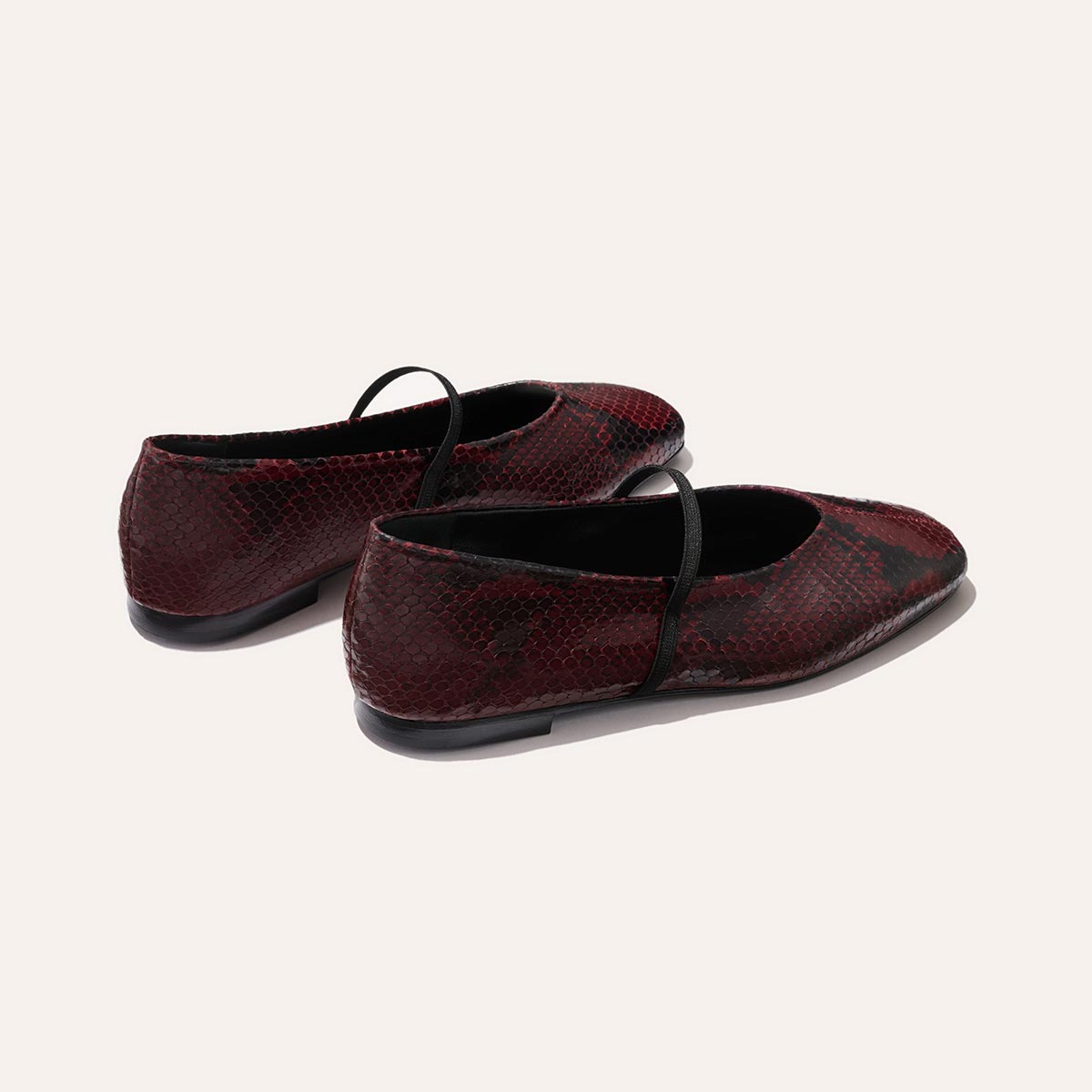 The Phoebe by margaux-development: burgundy python-embossed Mary Jane flats with black straps, sacchetto construction for superior comfort, shown from the back and side on a light background.