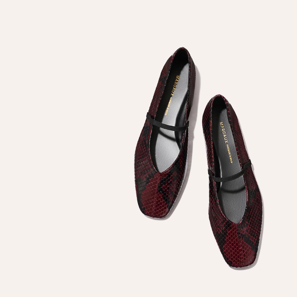 The Phoebe - Burgundy Python Embossed by margaux-development: burgundy and black snakeskin-patterned Mary Jane flats with a single black strap, sacchetto construction for plush comfort, shown on a light beige background.
