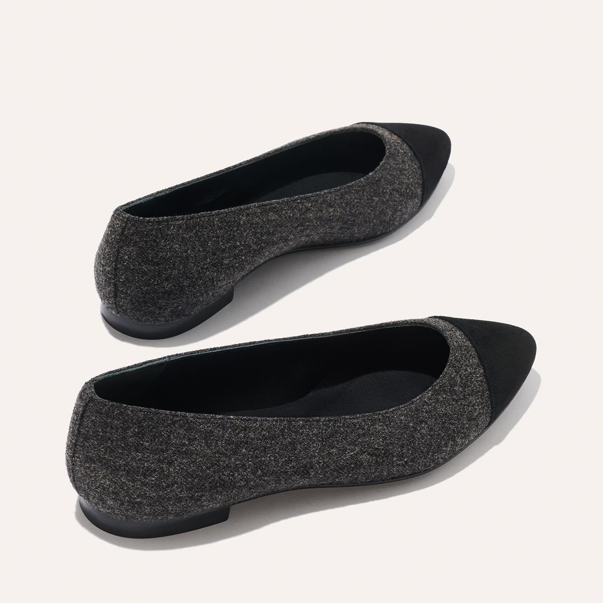 A pair of The Pointe - Grey Flannel flats by margaux-development, featuring dark gray textured fabric, solid black toe caps, and a sleek silhouette, displayed on a light background.