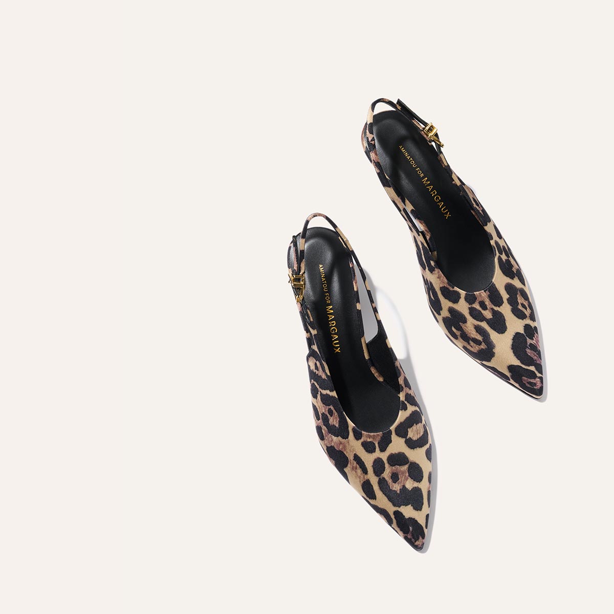 The Prado Sling - Leopard Satin by margaux-development features pointed toes, a beige and brown leopard print, black insoles, and gold buckles, shown against a light background.