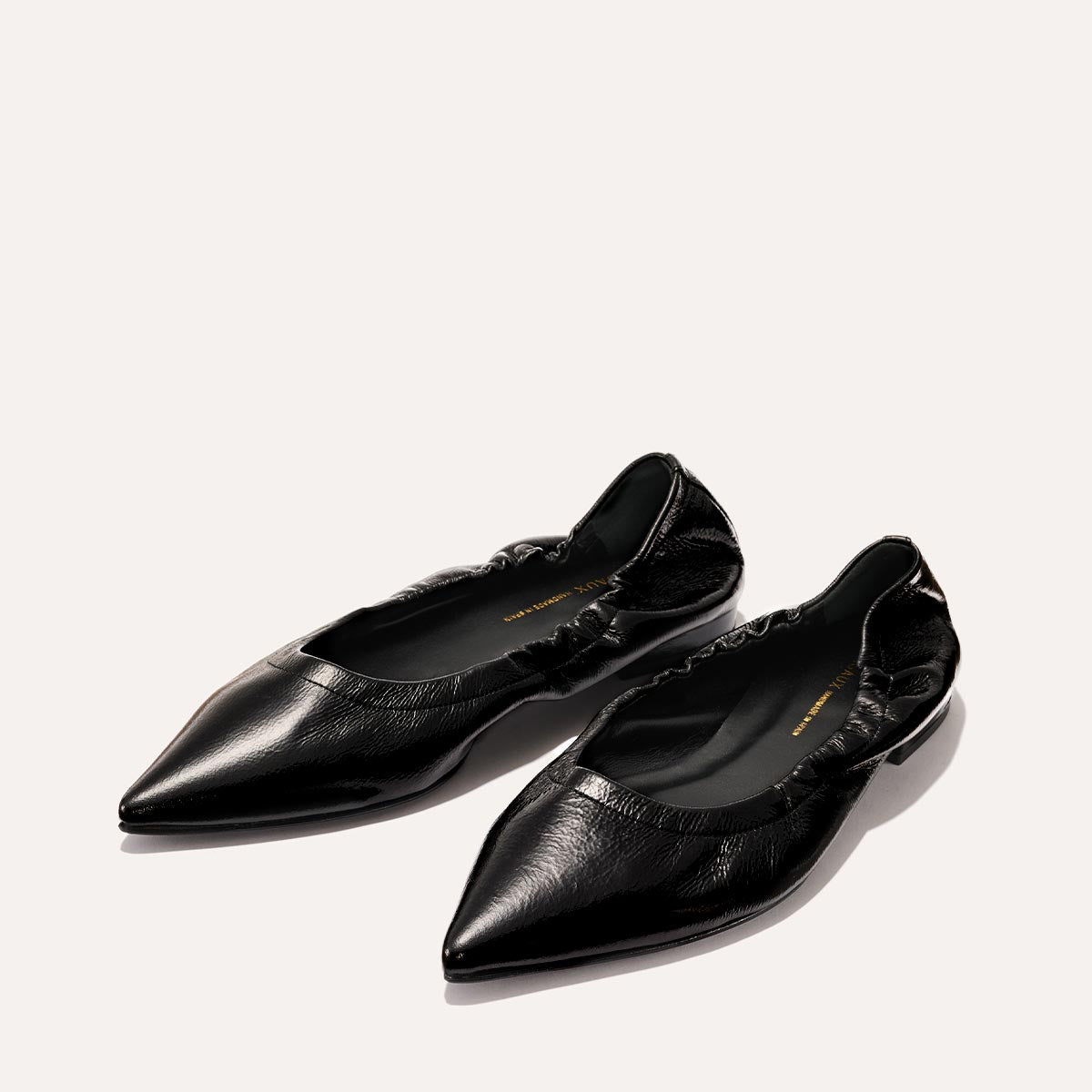 The Roma - Black Crinkle Patent by Margaux: black pointed-toe ballet flats with a ruched, elasticized opening, shown on a light background.