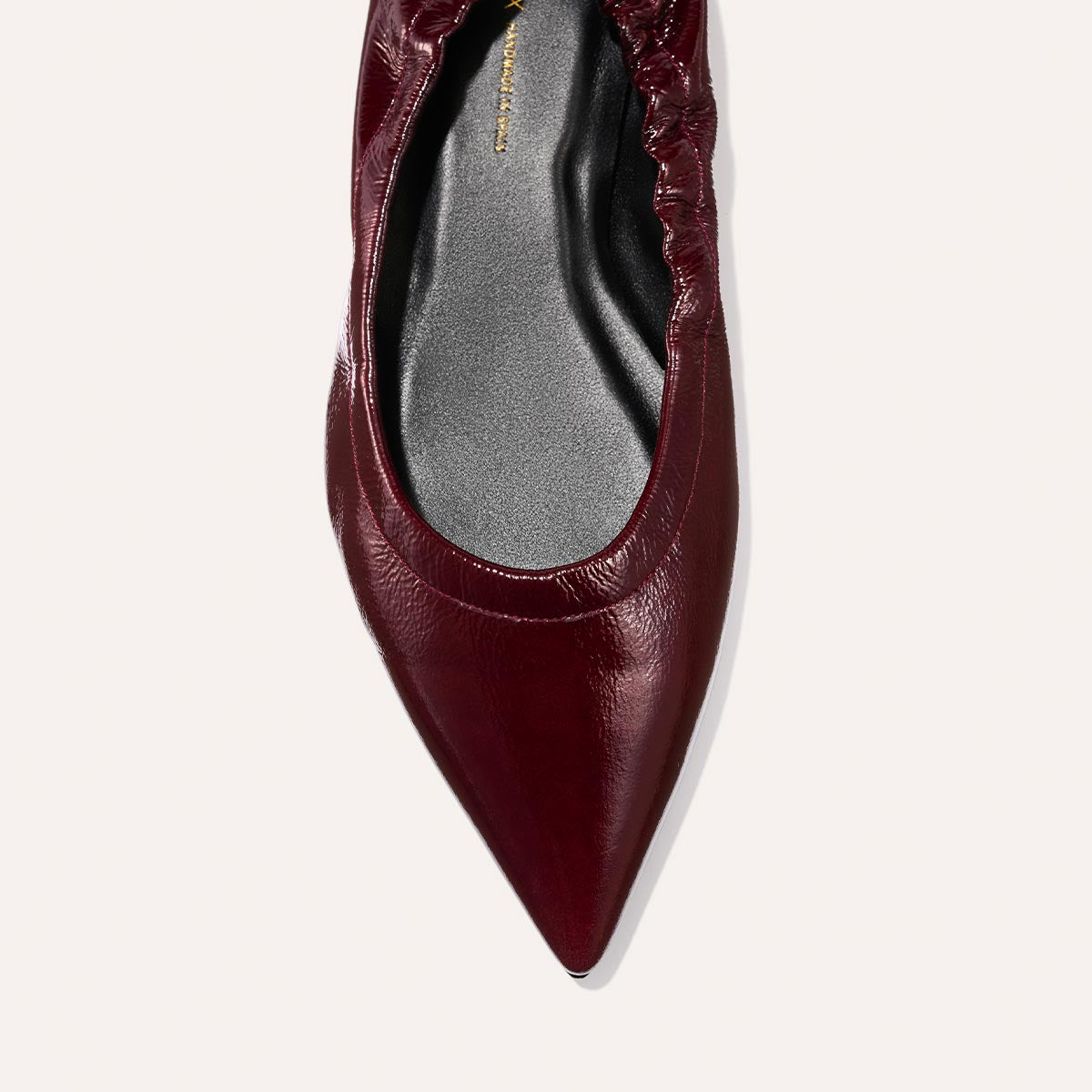 Close-up of Margaux’s The Roma - Merlot Crinkle Patent, a single pointed-toe ballet flat in burgundy patent leather with a textured crinkle finish and elastic detailing around the opening, photographed from above on a plain light background.