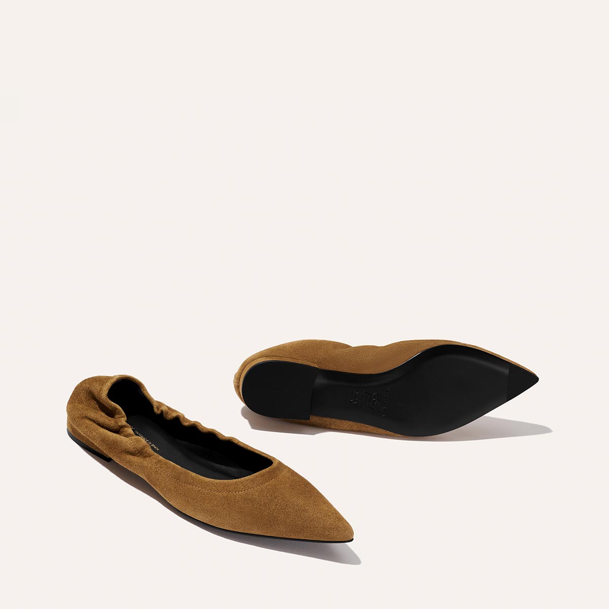 A pair of Margaux's "The Roma - Cedar Suede" pointed-toe ballet flats with ruched back detail, one flat and one on its side showing the black sole, displayed against a plain light background.