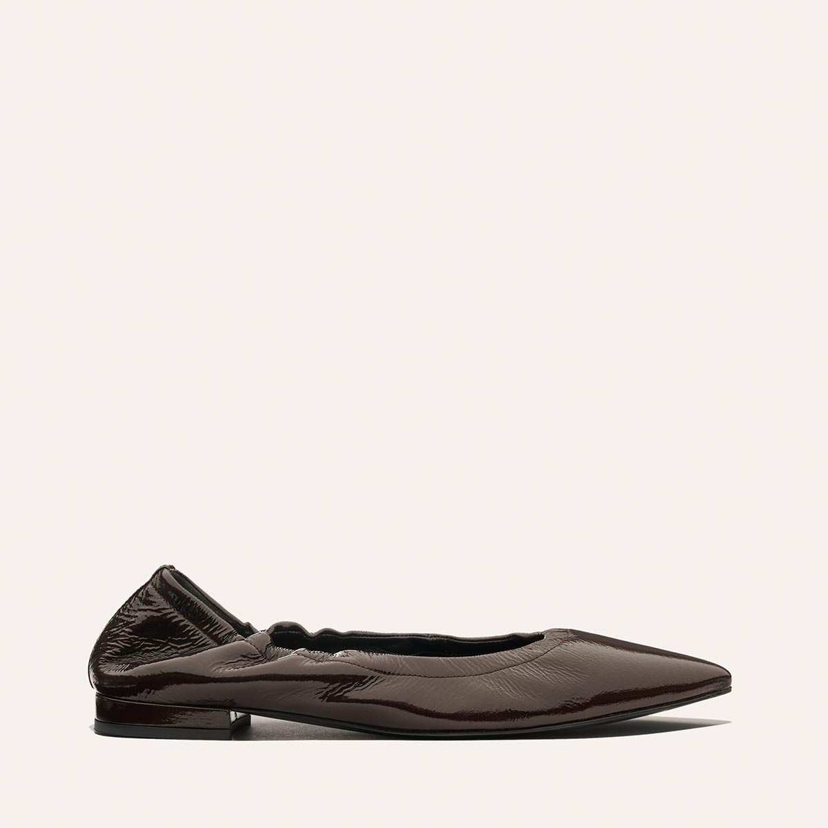 The Roma - Cocoa Crinkle Patent by Margaux is a dark brown, shiny pointed-toe ballet flat with a ruched heel and low square heel, shown against an off-white background.