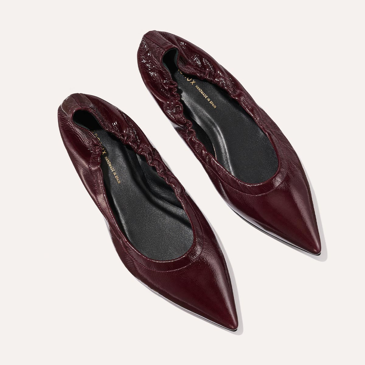 The Roma - Merlot Crinkle Patent by Margaux: chic pointed-toe ballet flats in burgundy with gathered elastic edges and black insoles, shown on a light background.
