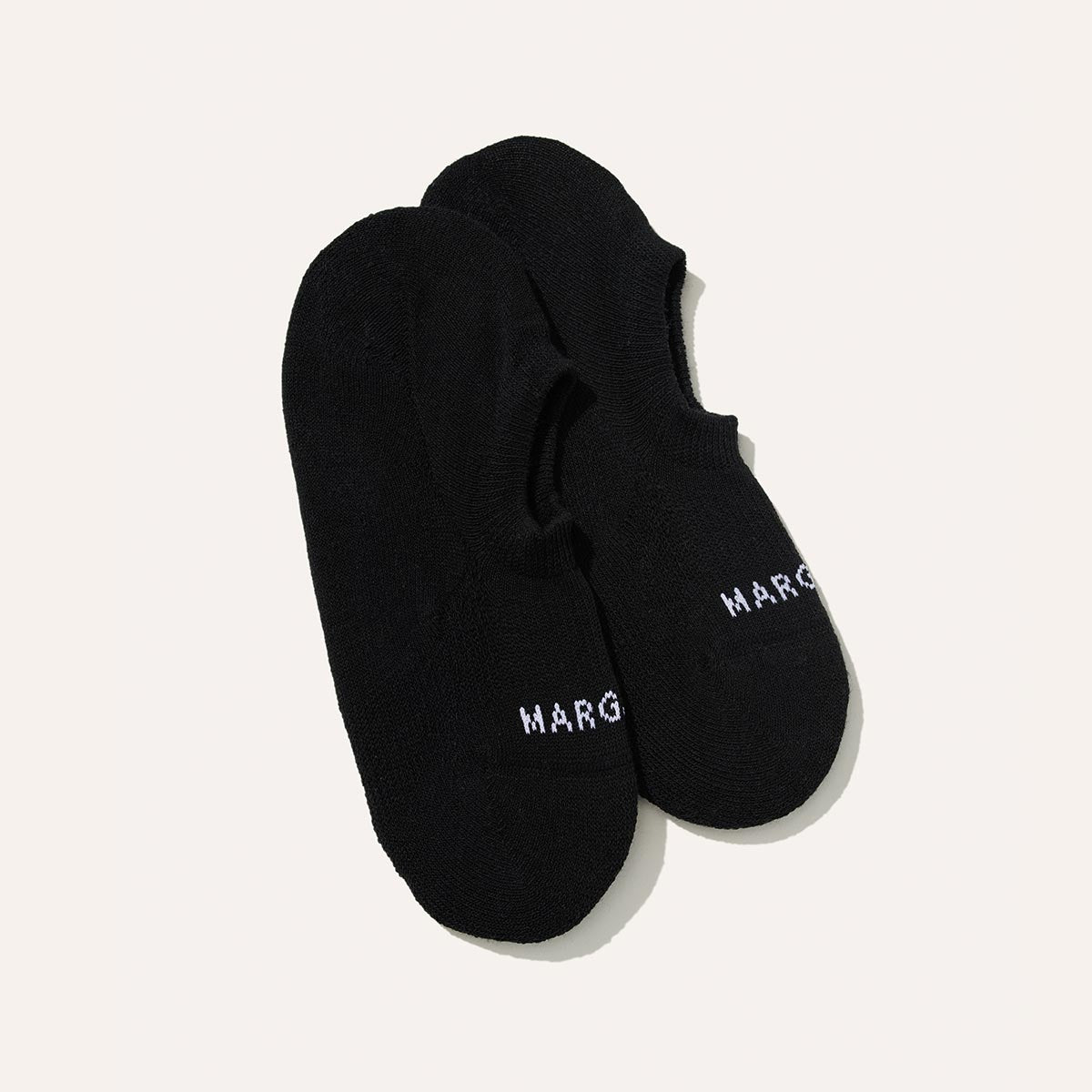 A pair of The Sneaker Sock - Black by Margaux, featuring non-slip grips and MARG embroidered in white near the toe, displayed on a plain light background.