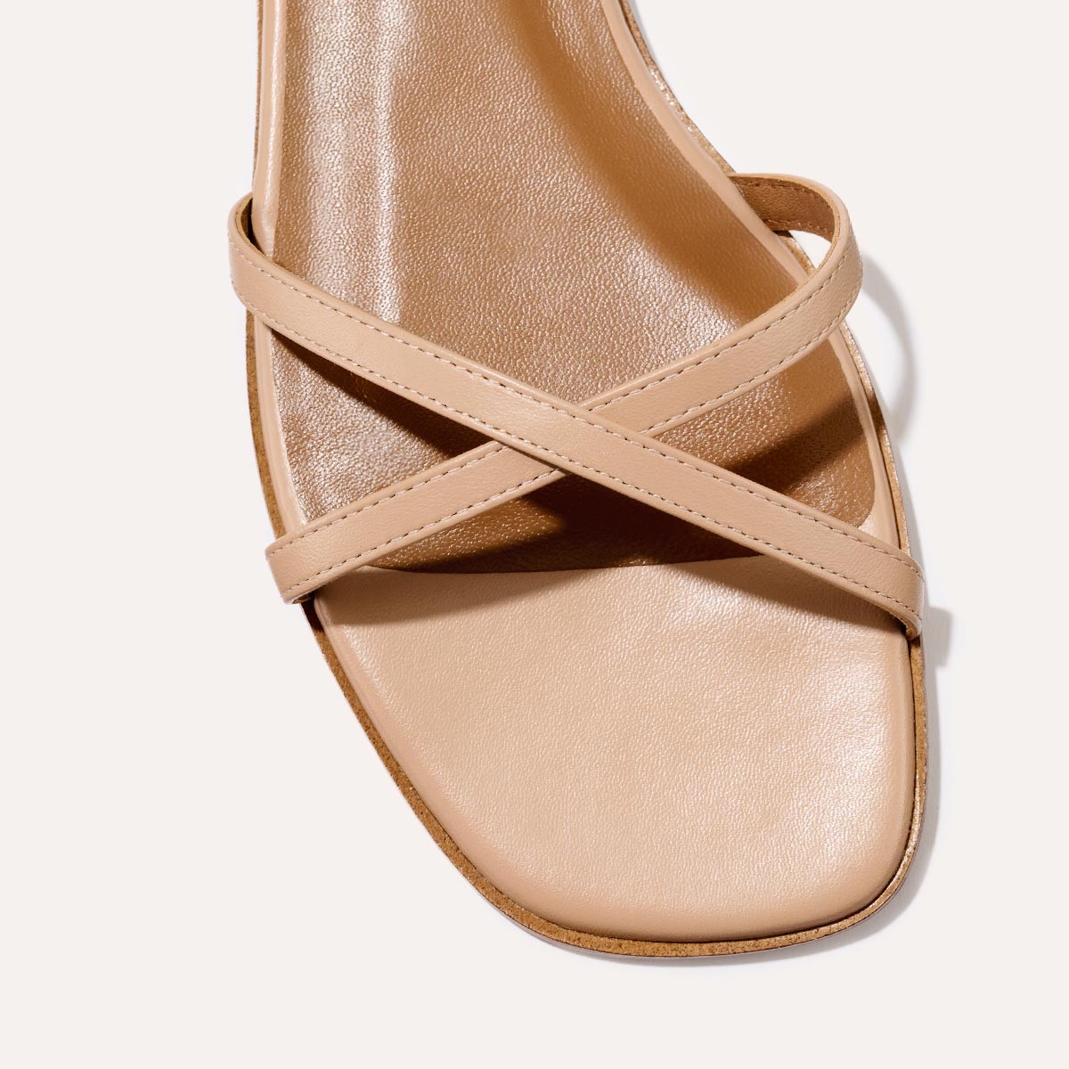 Close-up of The Wrap Sandal - Rose Nappa by Margaux, a sophisticated beige sandal with a square toe and two smooth leather crisscross straps, displayed on a neutral background.