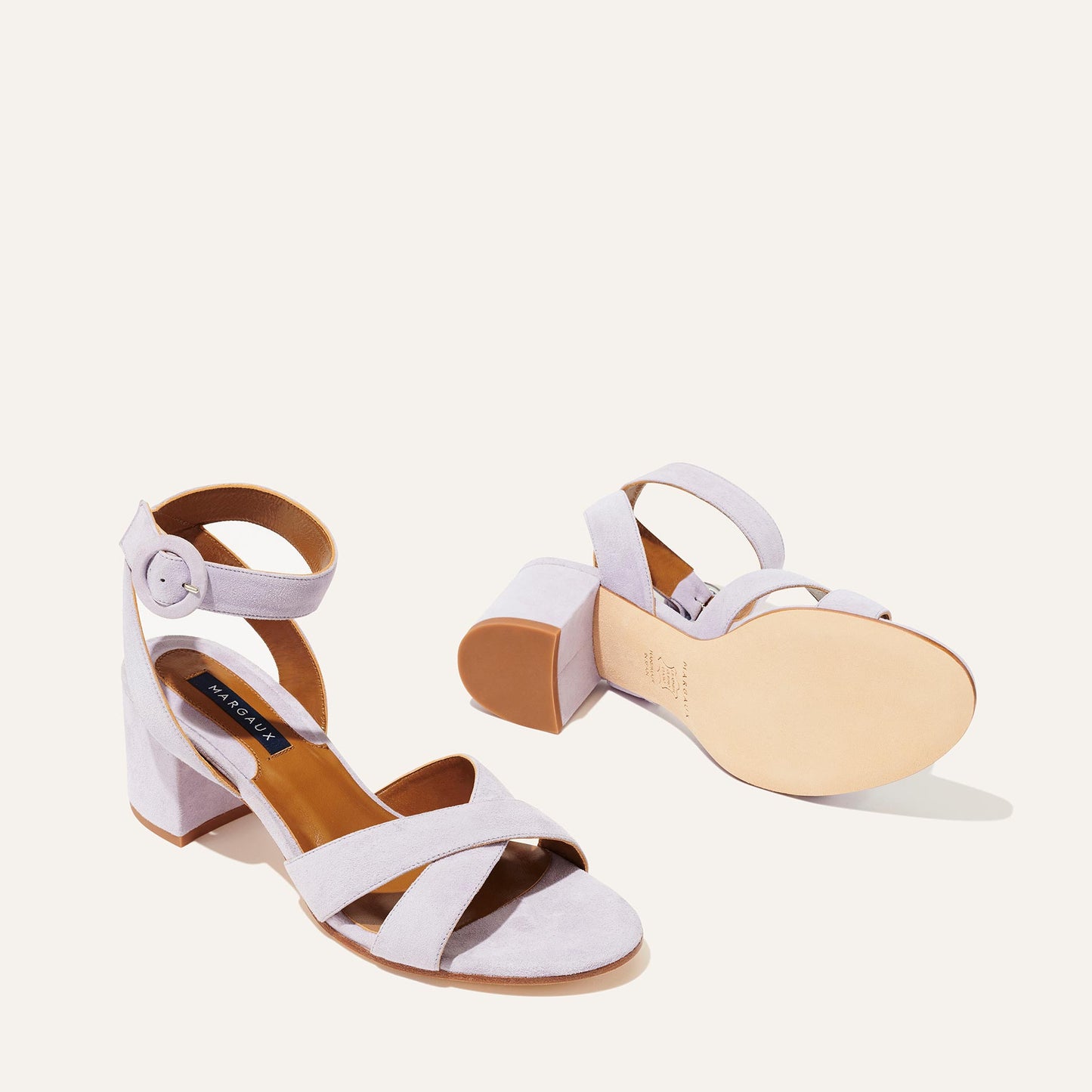 The City Sandal - Lilac Suede by margaux-development features light purple suede, block heels, crisscross straps, cushioned insoles, and ankle straps with round buckles, displayed from side and bottom angles on a light background.