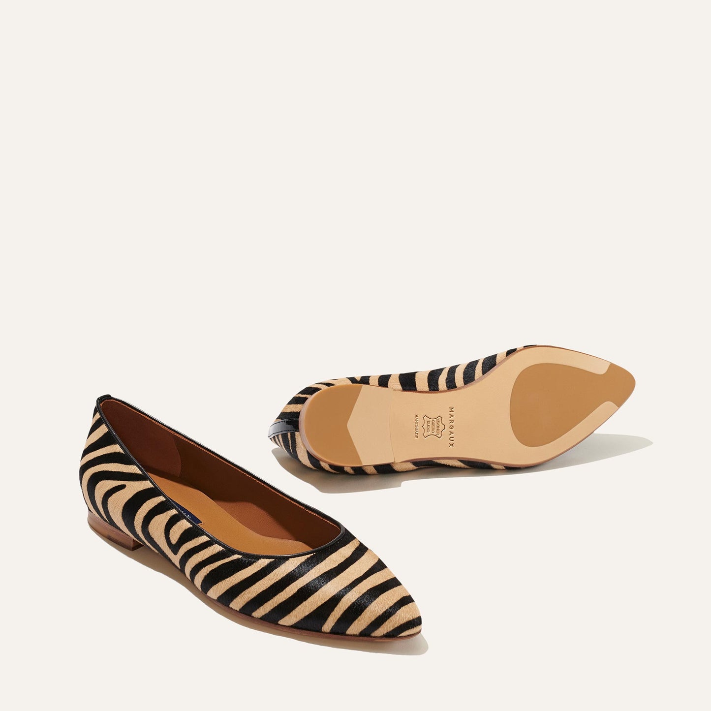Margaux’s The Pointe - Zebra Haircalf flats feature a sleek, pointed-toe silhouette with bold black and beige zebra stripes—a style so chic it’s worthy of Marie Claire. One shoe reveals the side and top, while the other shows its sole and small heel.