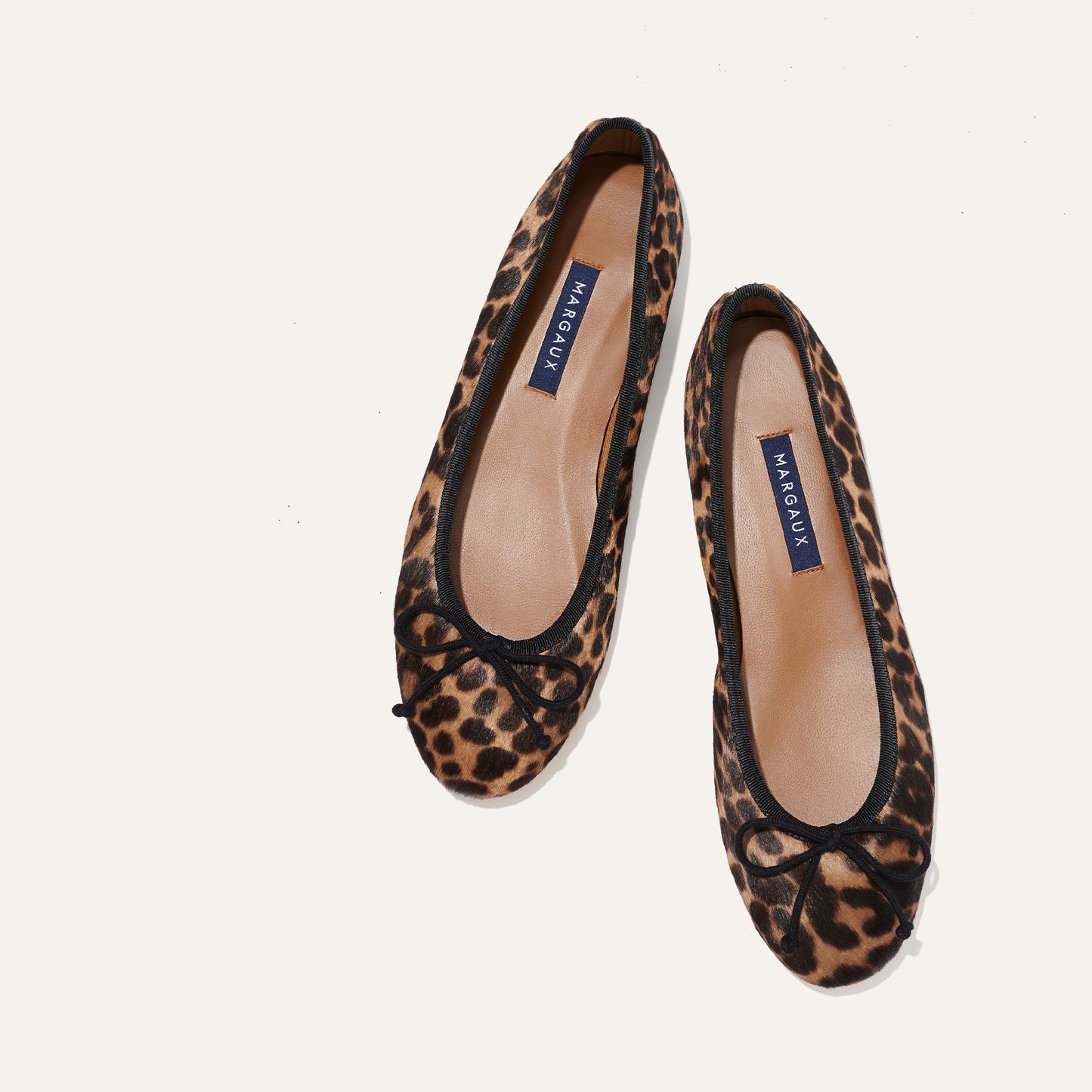 The Demi - Chocolate Leopard Haircalf by margaux-development: handmade in Spain, these leopard print ballet flats feature black trim and small front bows, shown on a white background.