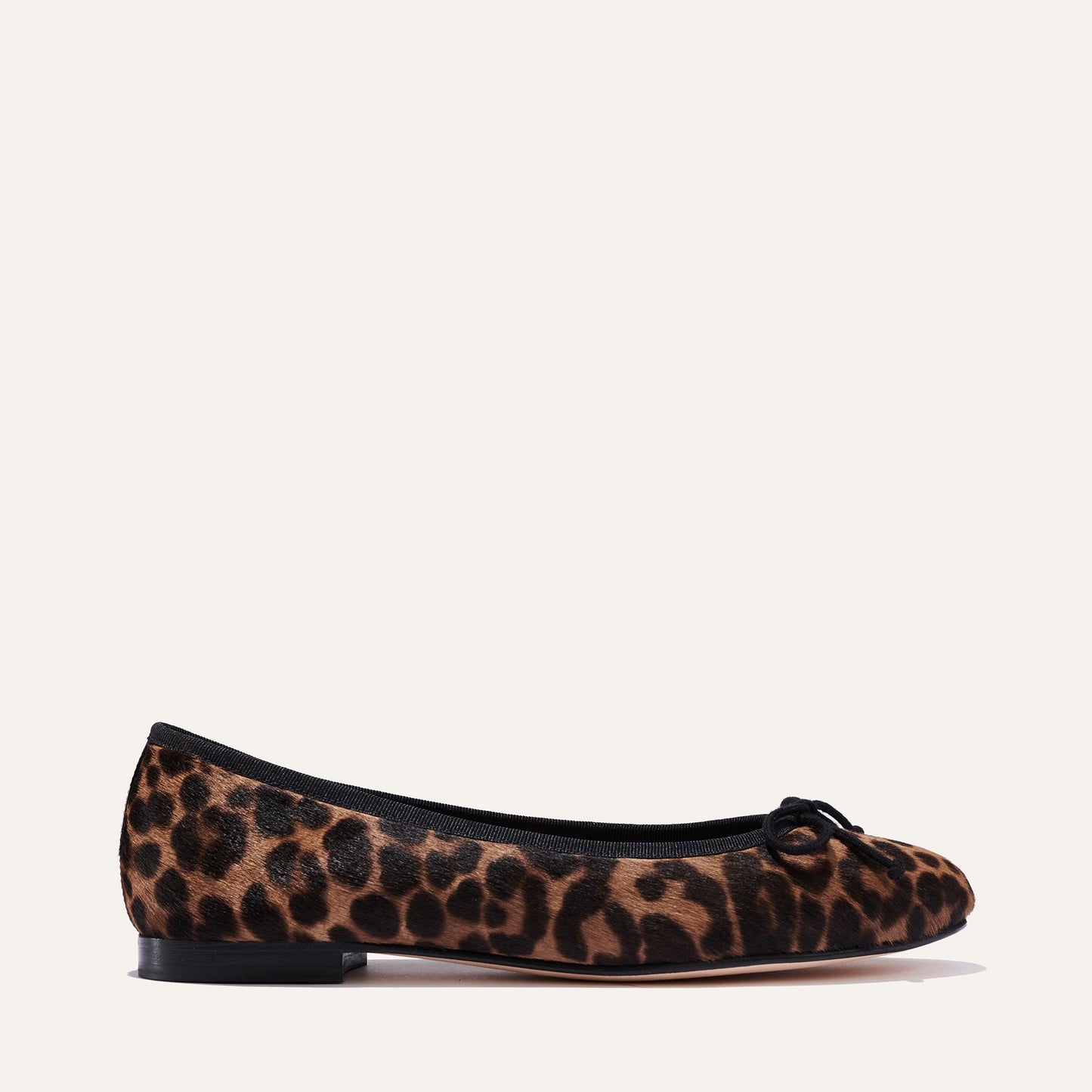 The Demi - Chocolate Leopard Haircalf by margaux-development: a handmade Spanish ballet flat in leopard print, featuring black trim and a bow at the toe, shown side profile on an off-white background.