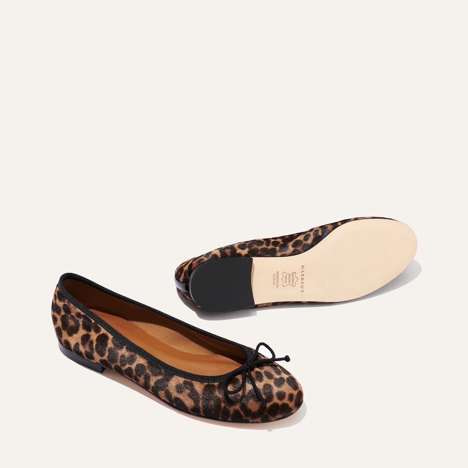 The Demi - Chocolate Leopard Haircalf by margaux-development features leopard-print ballet flats with black bows; one reveals the top view, the other highlights the beige branded sole, showcasing quality comfort and artisan Spanish craftsmanship.