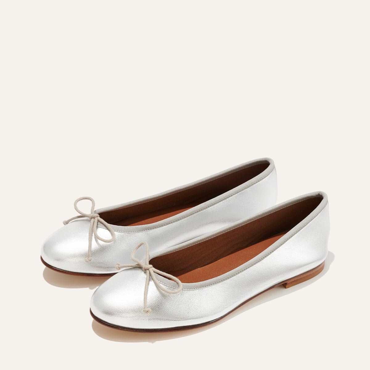 The Demi in metallic Silver Nappa, a comfortable ballet flat with a rounded toe and adjustable cord bow detail.