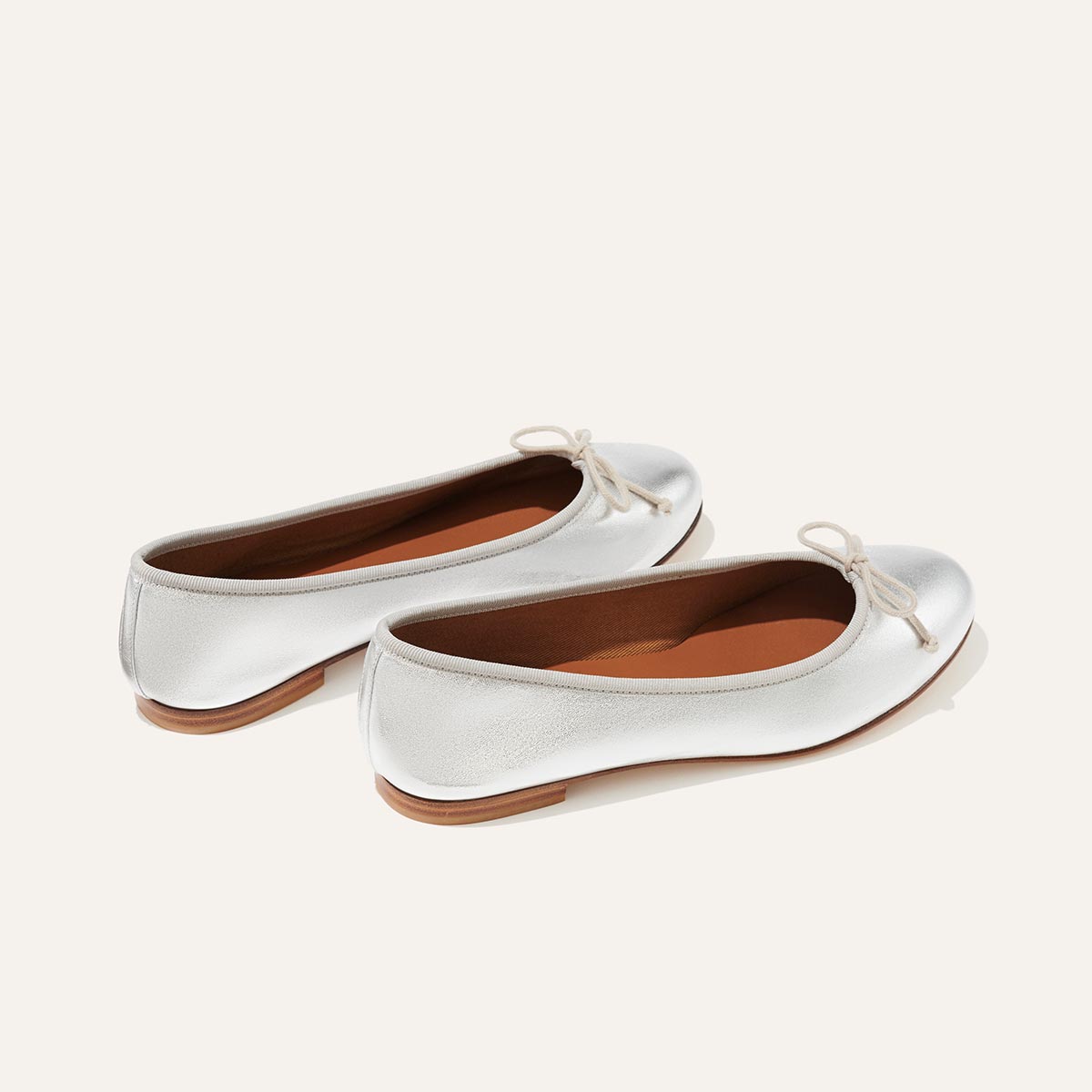 The Demi in metallic Silver Nappa, a comfortable ballet flat with a rounded toe and adjustable cord bow detail.