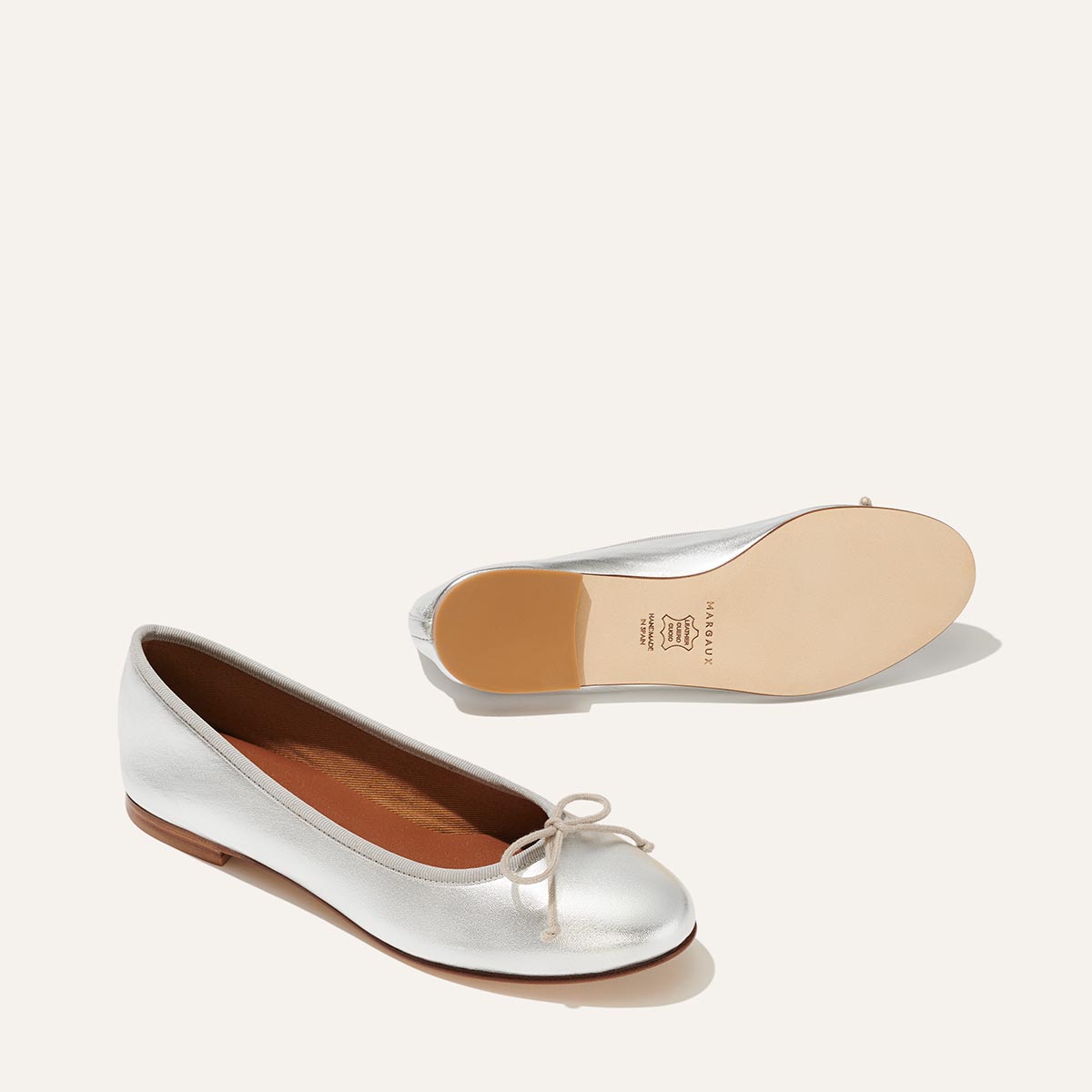 The Demi in metallic Silver Nappa, a comfortable ballet flat with a rounded toe and adjustable cord bow detail.