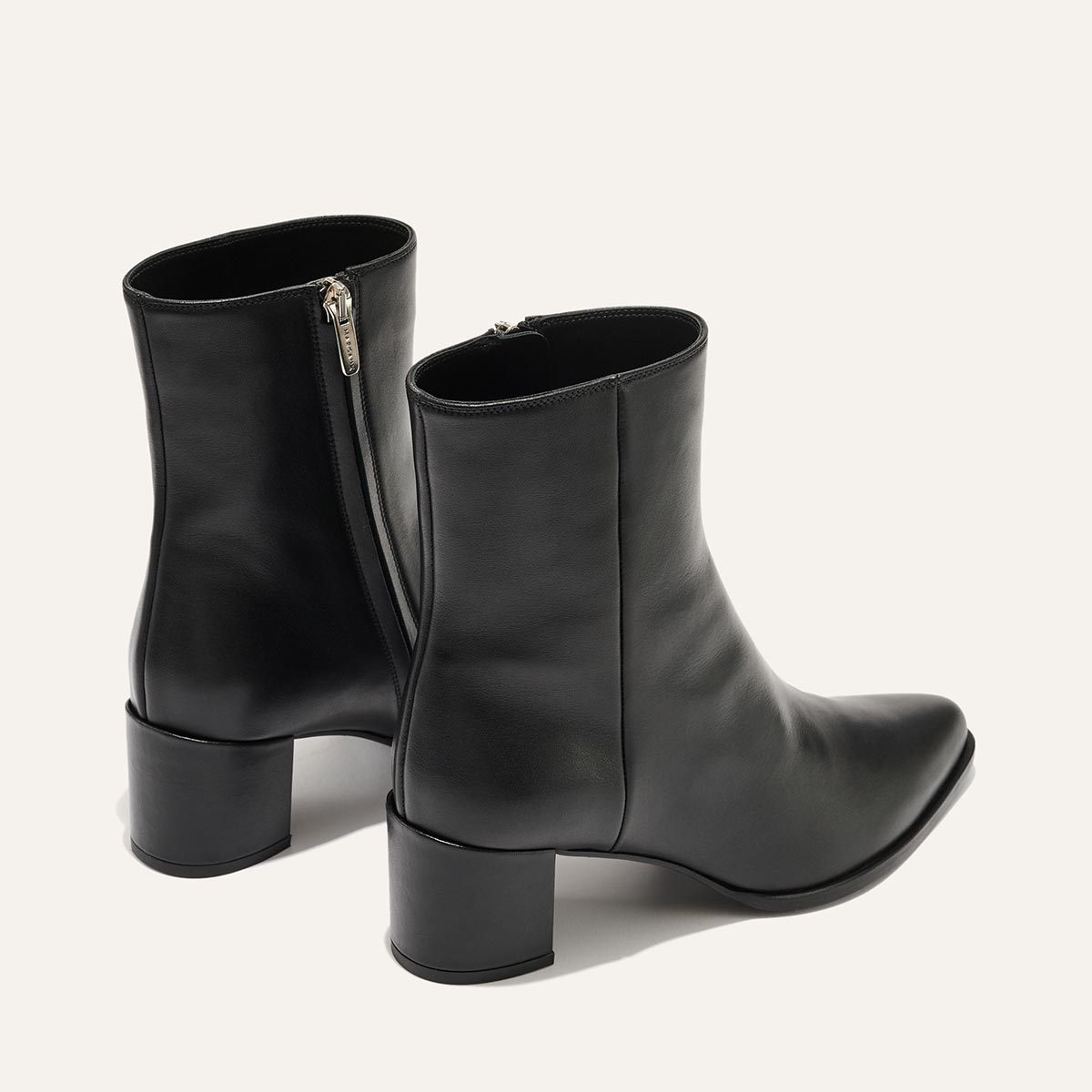 The Downtown Boot - Black Calf by Margaux is a sleek pair of black leather western ankle boots with low block heels and side zippers, shown against an off-white background.