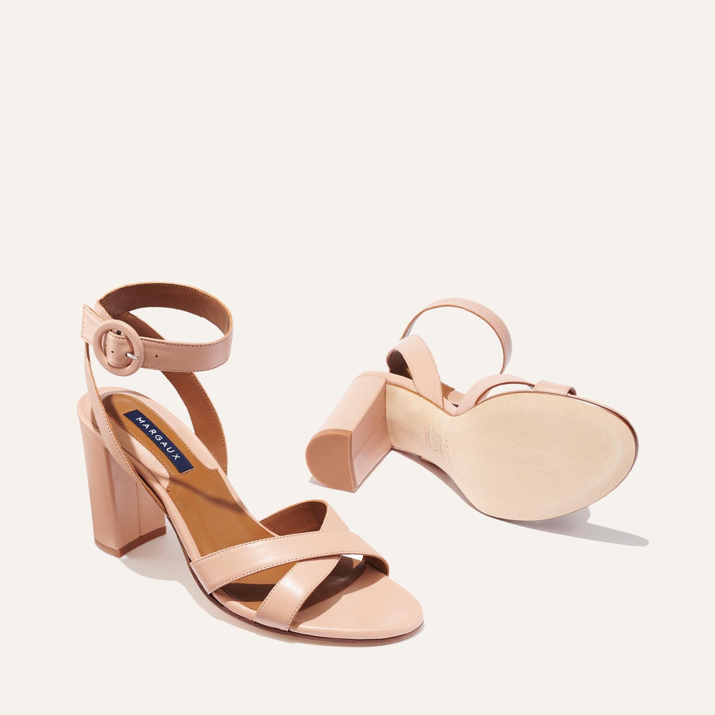 A pair of The Uptown Sandal - Rose Nappa by margaux-development with block heels, ankle straps, and a round buckle—one upright to show the buckle, the other on its side to reveal the sole, perfect for all-day comfort.