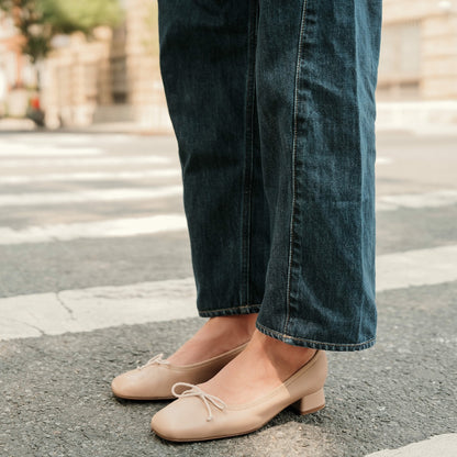 Person wearing blue jeans and beige shoes on a street.