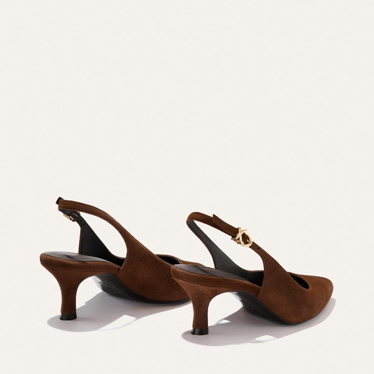 A pair of The Colette - Ganache Suede slingback heels by Margaux, featuring brown suede, a snip nose design, pointed toes, and gold buckles, displayed on a light background.