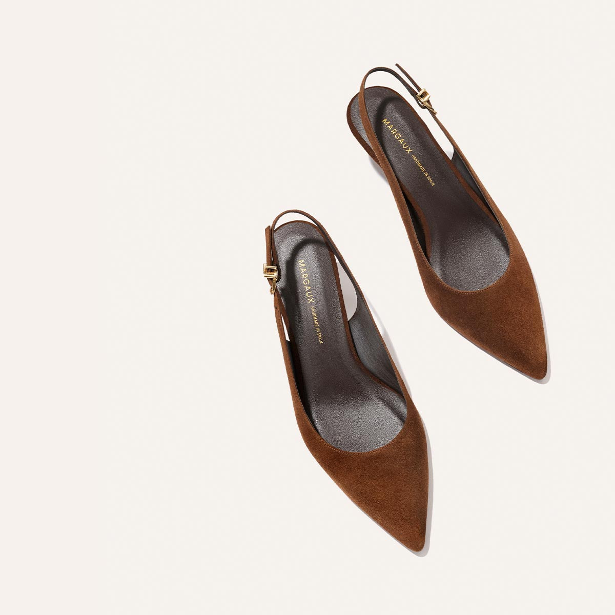 A pair of The Colette - Ganache Suede heels by Margaux, featuring brown suede, snip nose toes, and adjustable slingback ankle straps, shown on a light background.