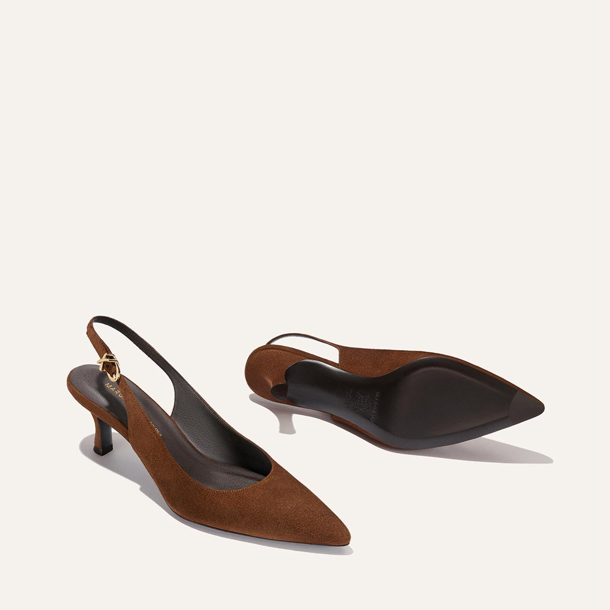 The Colette - Ganache Suede by Margaux: a pair of brown suede slingback heels with pointed toes, slender micro heels, and ankle straps accented with small gold buckles, displayed on a plain light background.