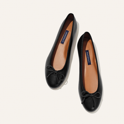 A pair of The Demi - Black Nappa ballet flats by margaux-development, handmade in Spain with tan insoles labeled MARGAUX and small bows on the toes, shown side by side on a light background.
