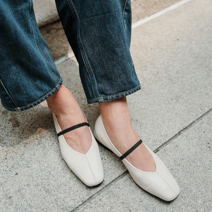 White flats with black straps worn with blue jeans on a concrete surface