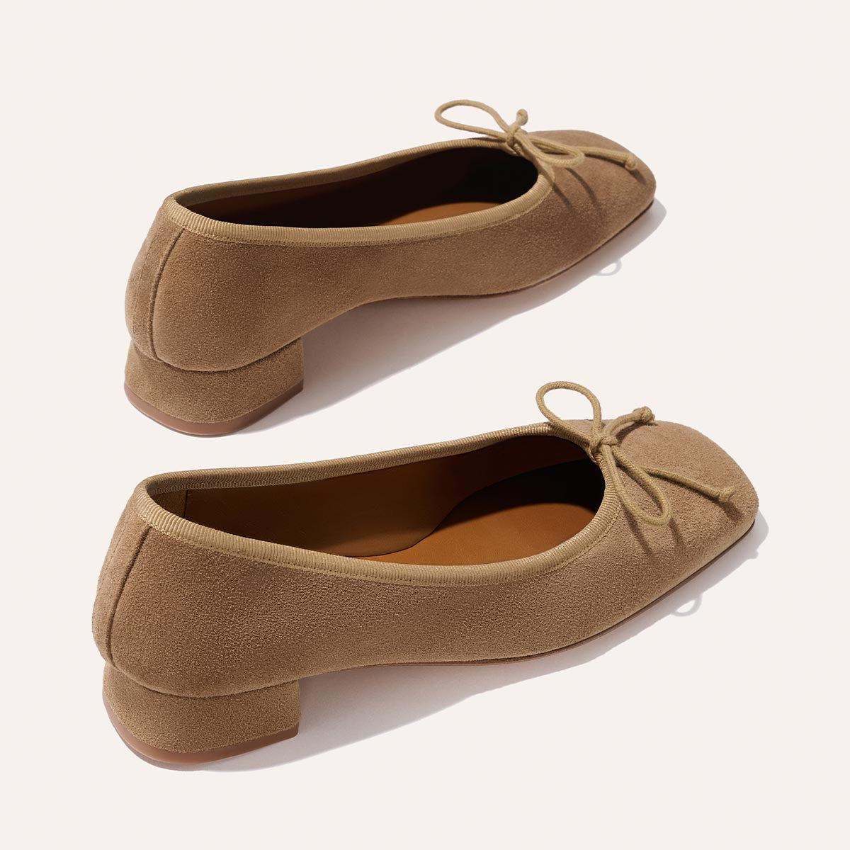 The Ada - Biscotti Suede by margaux-development is a tan suede ballet pump with a low heel, sacchetto construction, and front bow detail, shown against a light background.