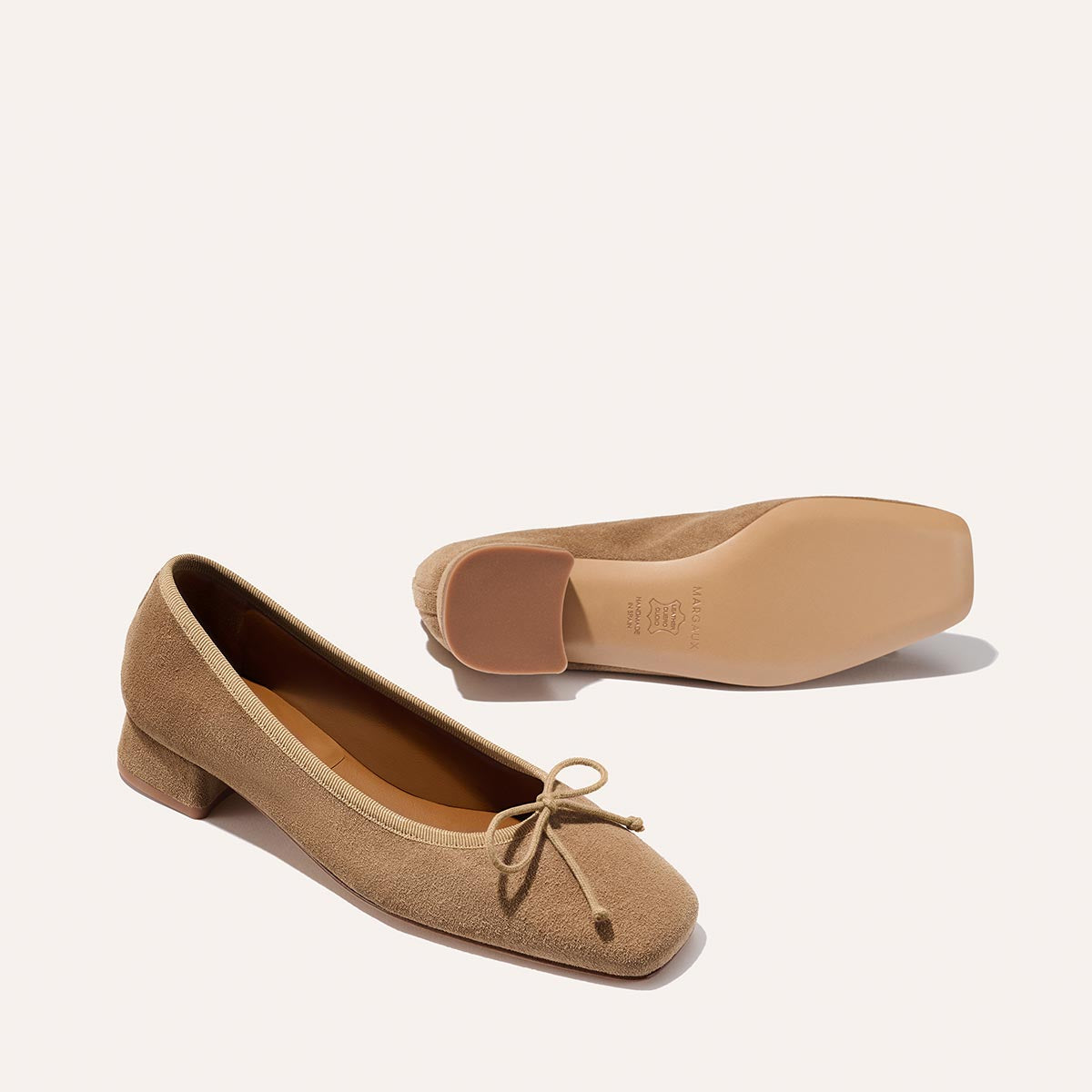 The Ada - Biscotti Suede by margaux-development: Tan suede low-heeled ballet pumps with bow accents and chic block heel, displayed on a white background—one shoe upright, the other on its side.