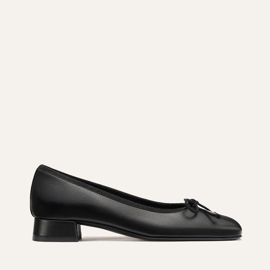 Introducing The Ada - Black Nappa by Margaux: a black leather ballet pump featuring a low block heel and a petite bow on the rounded toe, crafted with sacchetto construction and set against a plain light background.