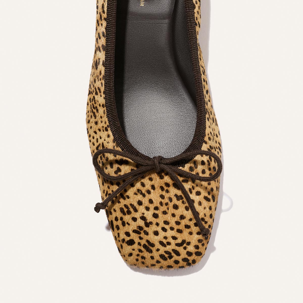 A close-up of The Ada - Tan Mini Cheetah Haircalf by Margaux, a square-toe ballet flat featuring a cheetah print pattern in haircalf, accented with black trim and a black bow at the front.