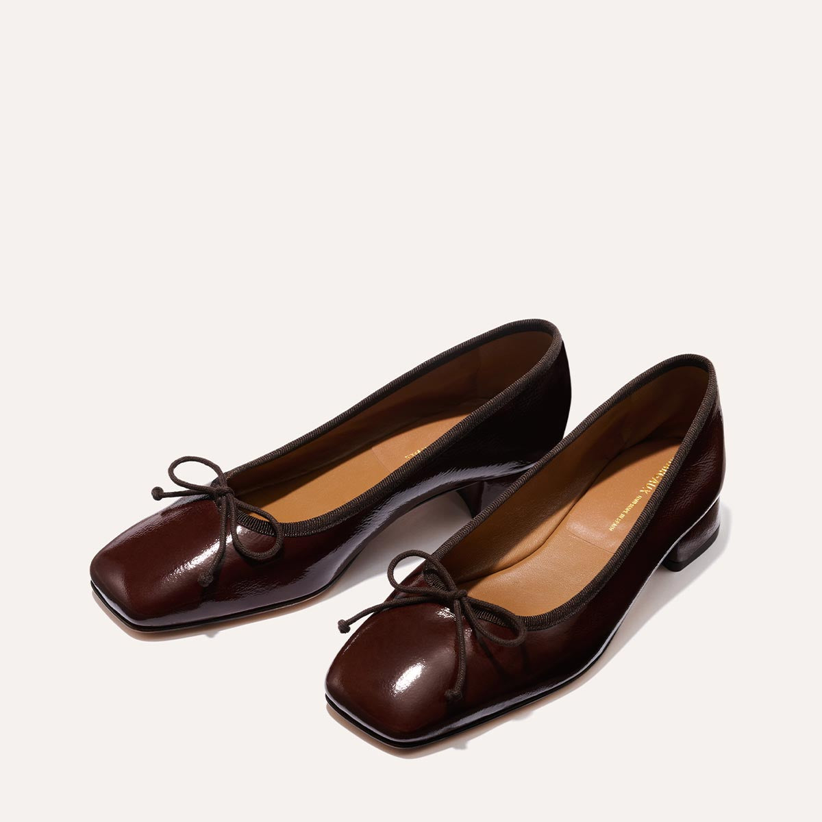 The Ada in Espresso Crinkle Patent, a comfortable ballet flat with a square toe, adjustable cord bow detail, and comfortable 1-inch block heel.