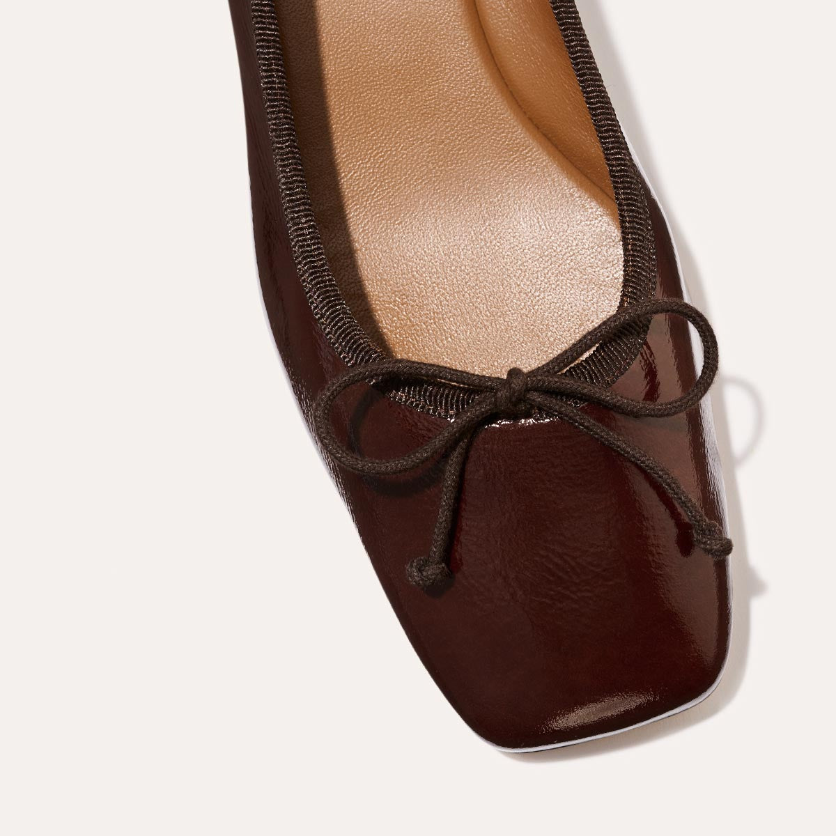 The Ada in Espresso Crinkle Patent, a comfortable ballet flat with a square toe, adjustable cord bow detail, and comfortable 1-inch block heel.