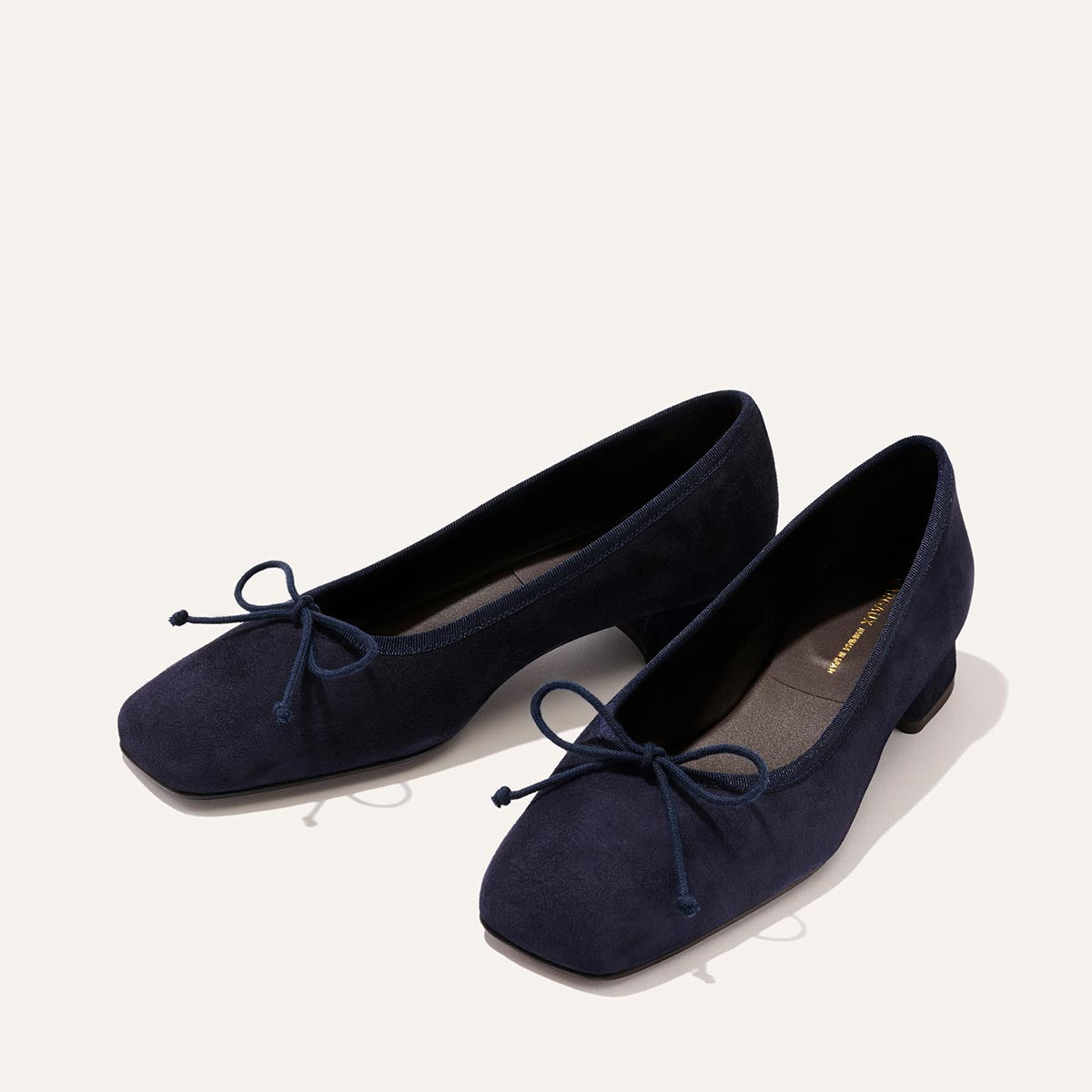 The Ada - Indigo Suede by Margaux: navy suede ballet pumps with low heels, square toes, and front bow details, designed for a glove-like fit, shown on a light background.