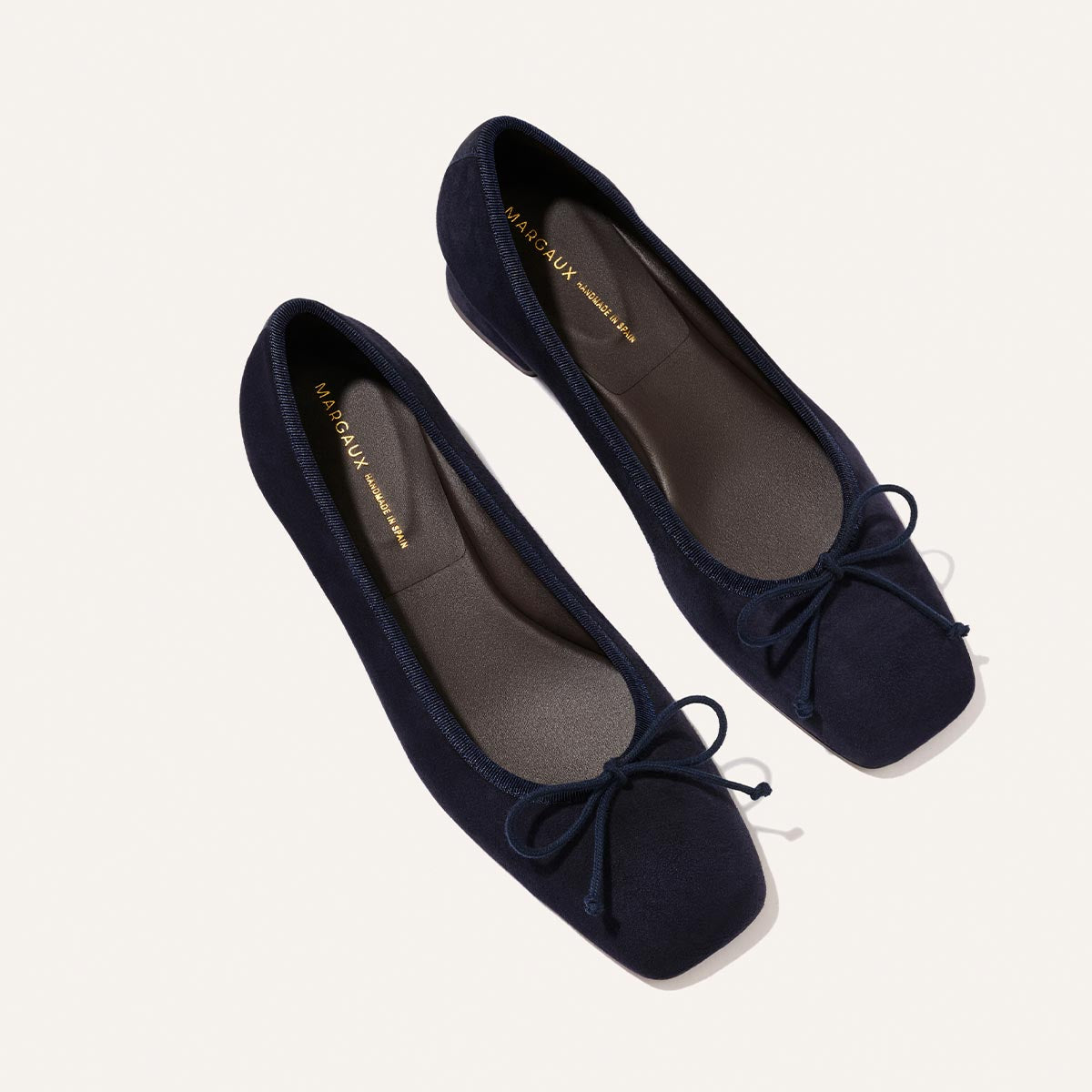 The Ada - Indigo Suede by Margaux are navy suede ballet flats with square toes, small front bows, and a glove-like fit, shown on a light background.