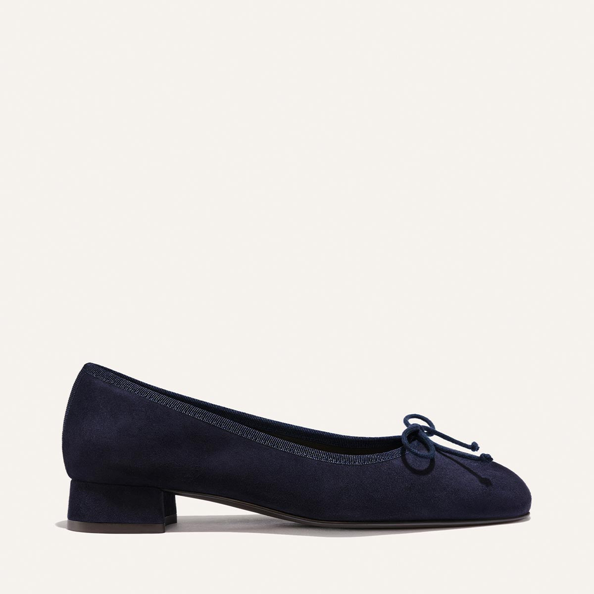 The Ada - Indigo Suede by Margaux: a navy blue suede ballet pump with low heel, rounded toe, and bow detail, designed for a glove-like fit. Shown on a plain light background.