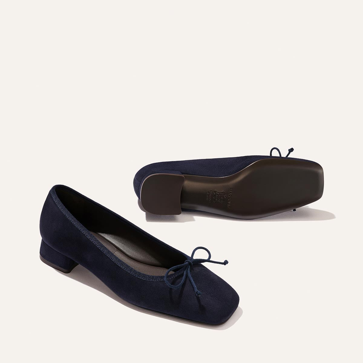 The Ada - Indigo Suede by Margaux: navy blue suede low-heeled ballet pumps with a glove-like fit, square toes, small front bows, and one shoe shown flipped to display its sole.