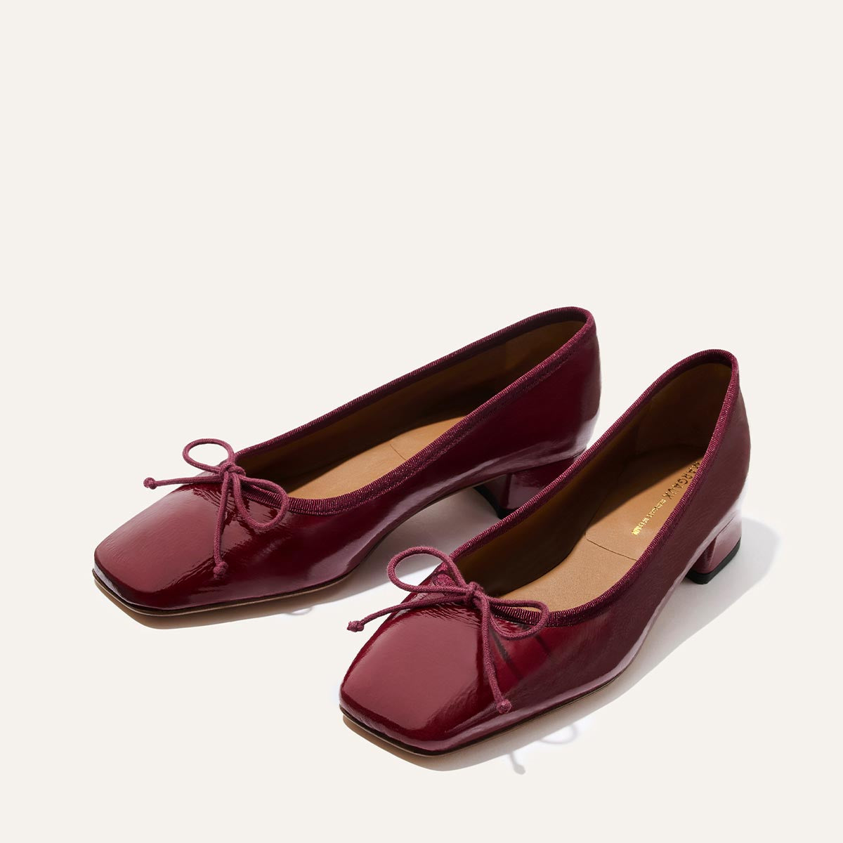 The Ada - Claret Crinkle Patent by margaux-development: glossy burgundy ballet pumps with low heels, square toes, and decorative bows, displayed on a light background for a classic look.