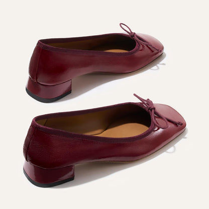 The Ada - Claret Crinkle Patent by margaux-development: burgundy patent leather low-heeled ballet pumps with square toes and small bow accents, shown on a neutral background.