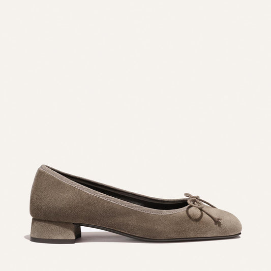 The Ada - Truffle Suede by Margaux is a taupe suede ballet flat featuring a low block heel, rounded toe, and a front bow with tassel detail. Its simple, elegant design makes it a timeless wardrobe staple.