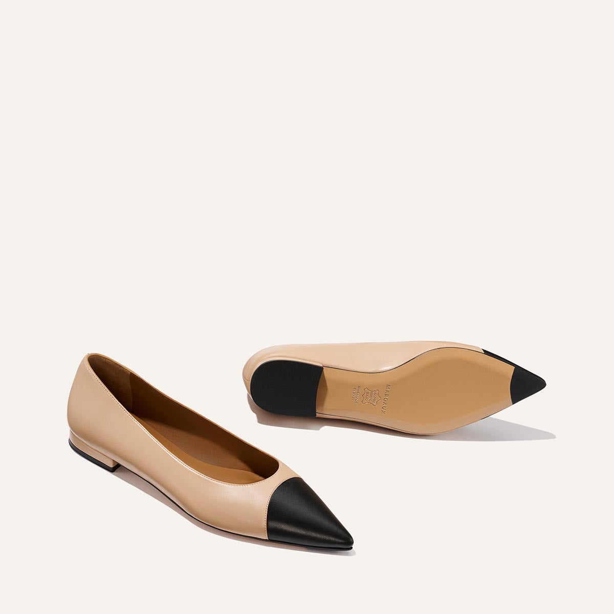 The Alba - Dune and Black Nappa by Margaux: beige pointed-toe ballet flats with black tips and a padded insole. One shoe stands upright, the other shows the sole, both set against a plain off-white background.